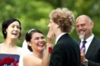 The bride's red lipstick left its mark on the groom at kissing time.  Half surprised and half amused, she tries to clean off his new matching lipstick.